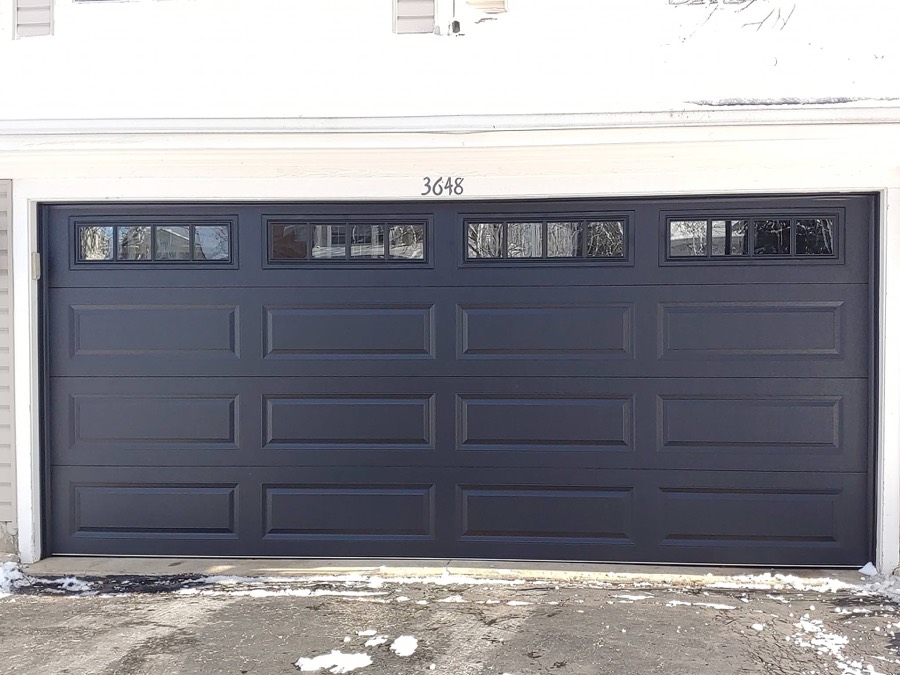New flush-panel black garage door installed on a suburban home